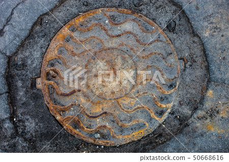 Manhole with rusty metal cover in cracked asphalt 50668616
