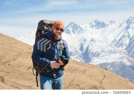 Portrait of smiling bearded male photographer in sunglasses against the background of snow-capped 50669965