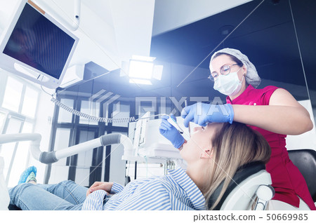 A professional dentist woman in glasses and overalls examines the oral cavity of a young girl in the 50669985