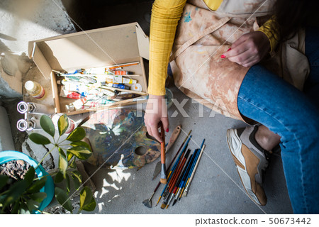 Young beautiful lady artist in apron with paint stains sitting on the floor in her studio 50673442