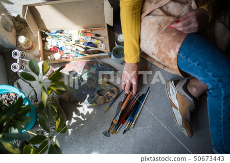 Young beautiful lady artist in apron with paint stains sitting on the floor in her studio 50673443