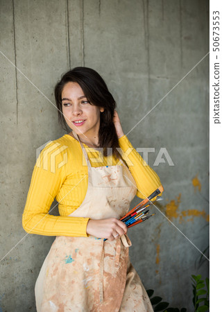 Young beautiful lady artist in apron with paint stains in her loft artistic studio Young beautiful lady artist in apron with paint stains in her loft artistic studio 50673553