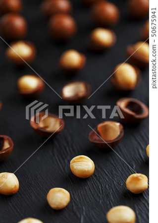 Purified and shell repeats macadamia nuts on black textural stone background. Healthy eating concept Purified and shell repeats macadamia nuts on black textural stone background. Healthy eating concept 50675941