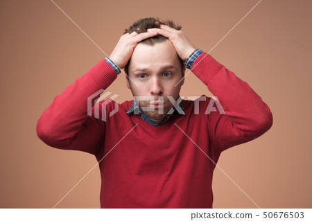 Man in red sweater in terror, holding head Man in red sweater in terror, holding head 50676503