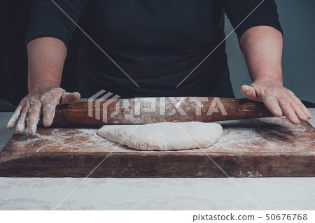 An old grandmother cleansing a dough with a shaft 50676768
