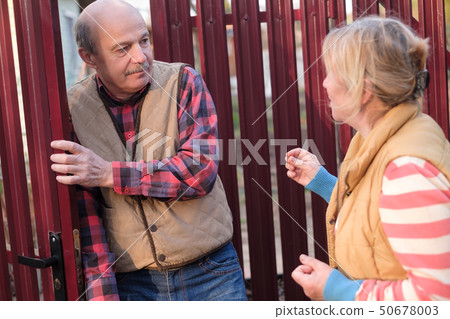 Woman is quarreling and having conflict with her neighbour at fence door 50678003