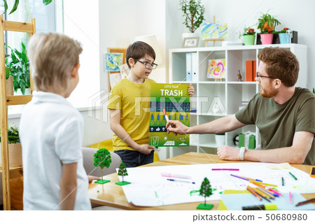 Attentive ginger teacher pointing on the element on educative poster 50680980