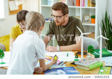 Concentrated bearded man in clear glasses sitting with his students Concentrated bearded man in clear glasses sitting with his students 50681028