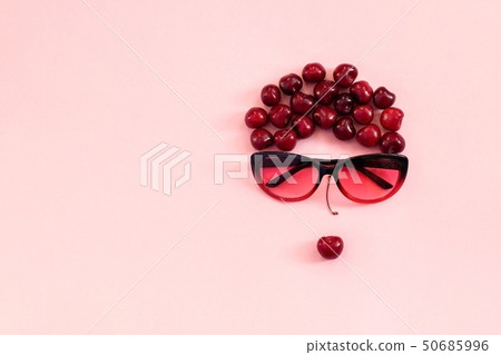 Red sweet cherry laid out in image of woman in sunglasses with lips on pink background. Concept 50685996