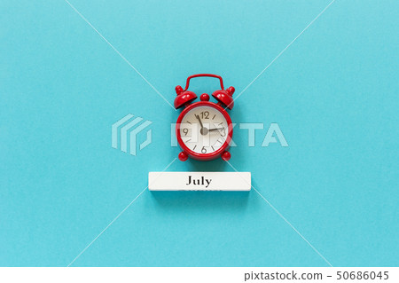 Wooden calendar summer month July and red alarm clock on blue paper background. Concept Hello July 50686045
