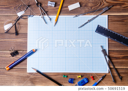 Graph paper with copyspace and student material on wooden table. Graph paper with copyspace and student material on wooden table. 50691519