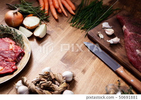 Two pieces of red meat next to fresh vegetables on rustic wooden table. 50691881