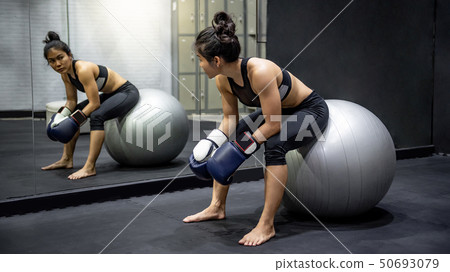 Asian girl boxer sitting on exercise ball in gym Asian girl boxer sitting on exercise ball in gym 50693079
