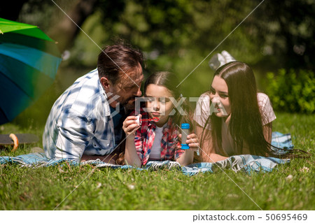 Family Lying On The Blanket In The Park. Daughter Holding Soap Bubbles. Family Lying On The Blanket In The Park. Daughter Holding Soap Bubbles. 50695469