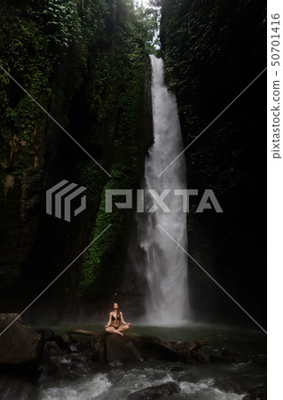 Beautiful young woman meditating in lotus position while doing yoga in a wonderful forest near 50701416