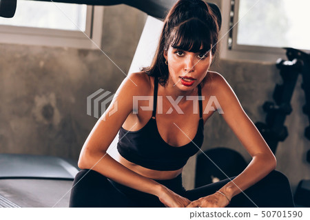 Young sweaty woman sitting on treadmill in gym Young sweaty woman sitting on treadmill in gym 50701590
