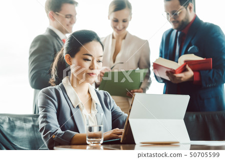 Asian business woman working on laptop with colleagues in background 50705599