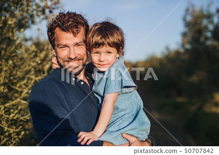 Father with small daughter standing outdoors by olive tree. Father with small daughter standing outdoors by olive tree. 50707842