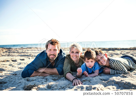 Young family with two small children lying down outdoors on beach. Young family with two small children lying down outdoors on beach. 50707858