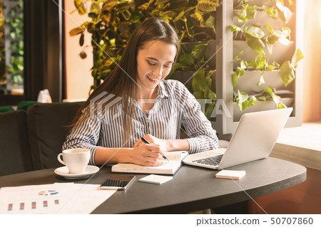 Young woman sitting at cafe in front of laptop and making notes 50707860