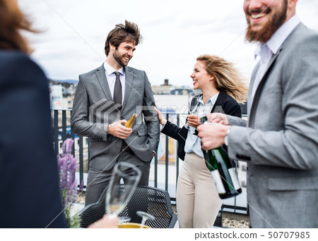 A group of joyful businesspeople having a party outdoors on roof terrace in city. A group of joyful businesspeople having a party outdoors on roof terrace in city. 50707985
