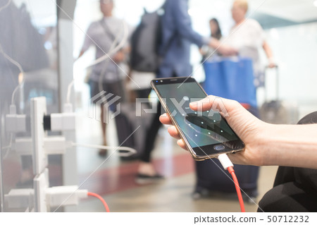 Female hands holding and using smartphone while charging it in a public place using electric plug 50712232