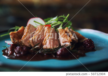 Duck confit with salad , baked apple and raspberry sauce served on wooden table 50712904
