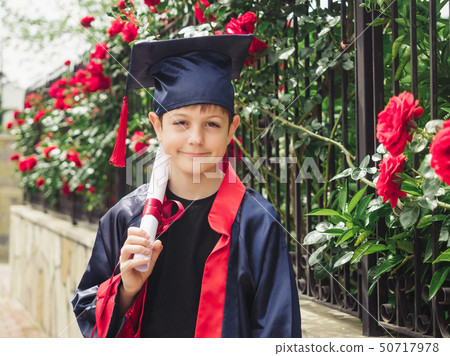 Happy caucasian child in graduation gown with diploma standing near stone fence full of wild roses Happy caucasian child in graduation gown with diploma standing near stone fence full of wild roses 50717978