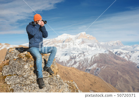 Portrait of a bearded traveler photographer in sunglasses and a cap sits on a rock with mirror Portrait of a bearded traveler photographer in sunglasses and a cap sits on a rock with mirror 50720371
