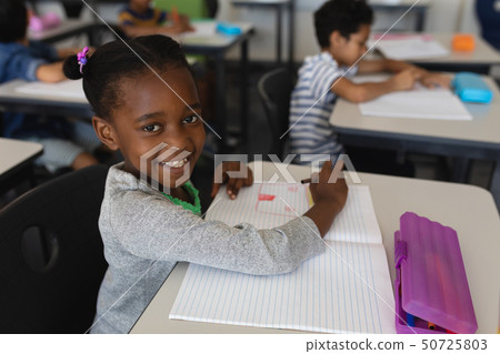 Schoolgirl looking at camera while studying in classroom 50725803