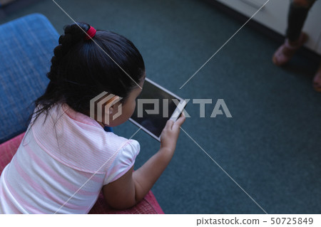 Schoolgirl studying on digital tablet while lying on the couch in school library Schoolgirl studying on digital tablet while lying on the couch in school library 50725849