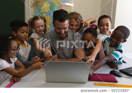 Male school teacher teaching schoolkid on laptop at desk in classroom 50725897