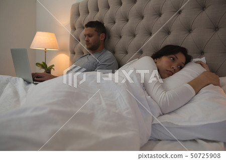 Man using laptop while woman sleeping in bedroom 50725908