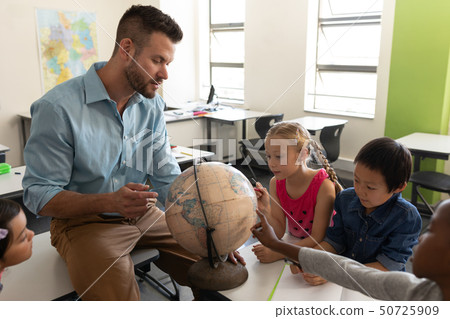 Side view of male teacher teaching his kids about geography by using globe in classroom 50725909