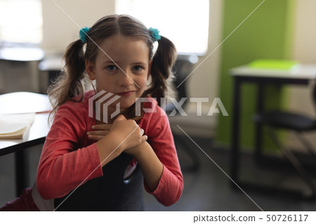 Front view of cute schoolgirl looking at camera and sitting at desk in classroom 50726117