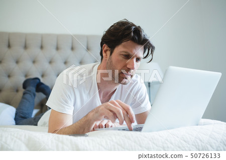 Man using laptop in bedroom 50726133