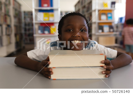 Happy schoolboy leaning his face on books and looking at camera on table Happy schoolboy leaning his face on books and looking at camera on table 50726140