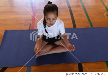 Schoolgirl doing yoga and meditating on a yoga mat in school Schoolgirl doing yoga and meditating on a yoga mat in school 50726342