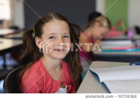 Schoolgirl looking at camera while sitting in classroom 50726368