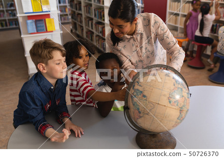 Female teacher teaching the kids about the globe at table in school library 50726370