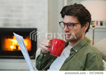 Man reading newspaper while having coffee in living room 50726686