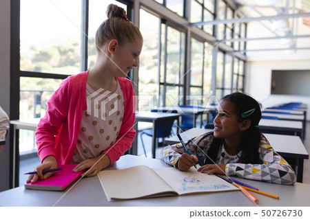 Schoolkids talking with each other at desk in classroom 50726730