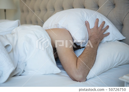 Man with pillow covering his face while sleeping in bedroom Man with pillow covering his face while sleeping in bedroom 50726750