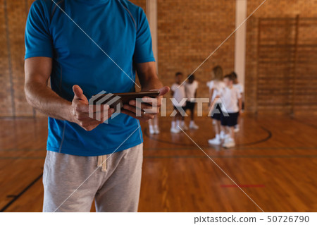 Mid section of basketball coach using digital tablet at basketball court 50726790
