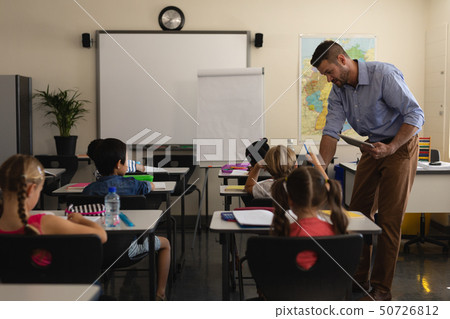 School teacher holding digital tablet and teaching in a classroom 50726812