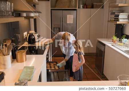 Mother with her daughter removing muffin cakes from oven in kitchen 50727060