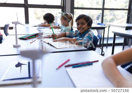 Schoolboy sitting at desk and looking at camera in classroom Schoolboy sitting at desk and looking at camera in classroom 50727198