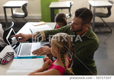 Young school teacher helping girl with study on laptop in classroom Young school teacher helping girl with study on laptop in classroom 50727207