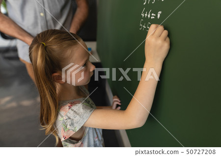 High angle view of schoolgirl writing on chalk board in classroom 50727208