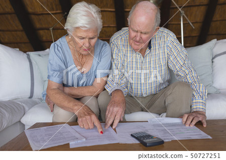 Senior couple discussing over medical bills in living room Senior couple discussing over medical bills in living room 50727251